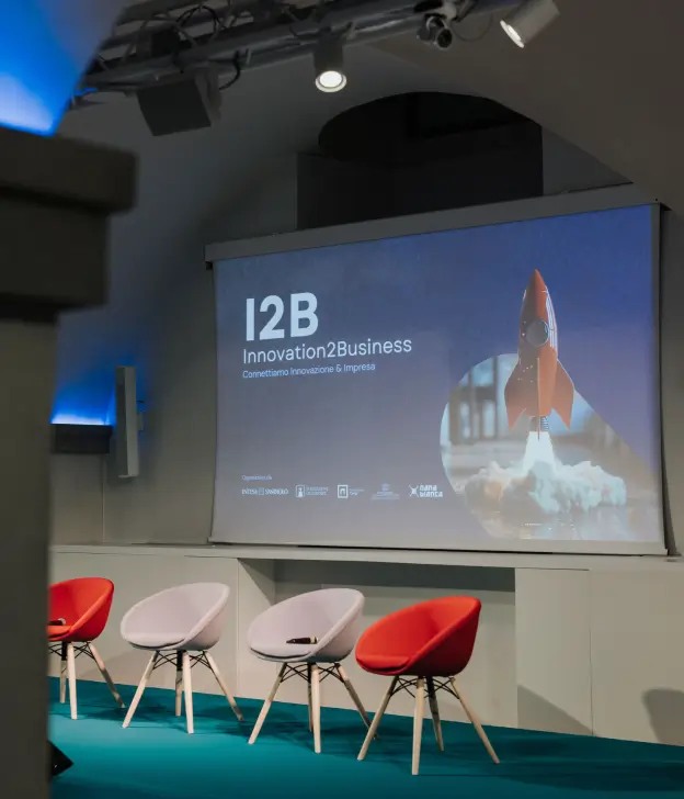 Allestimento della sala eventi per il programma I2B – Innovation2Business, con sedute e proiezione su maxi schermo, in una delle sale di Nana Bianca.