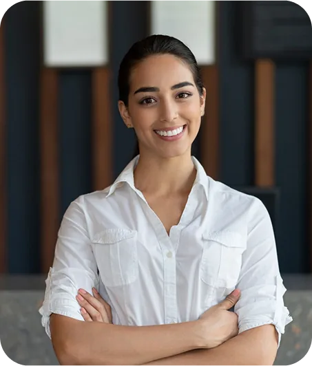 A woman in a white button-up shirt stands confidently with arms crossed, set against a modern, minimalist background.