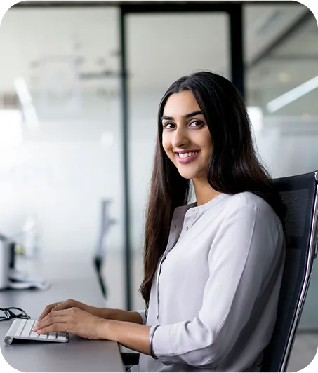 A person sits at a modern desk, typing on a laptop amidst an office environment, exuding focus and professionalism.