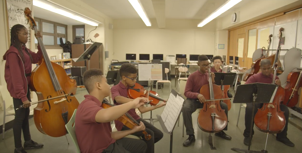 Students playing string instruments together in a school music classroom