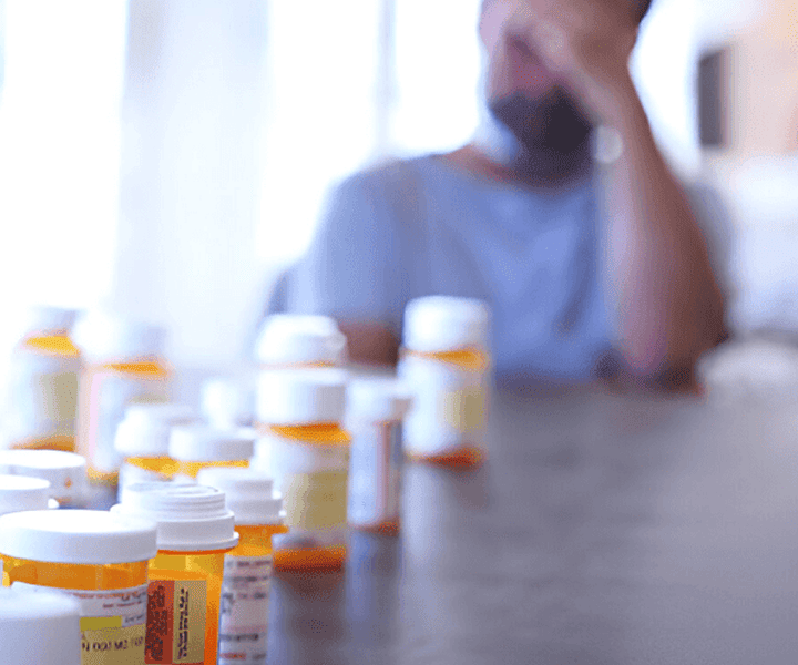 Man in front of many pills holding his head