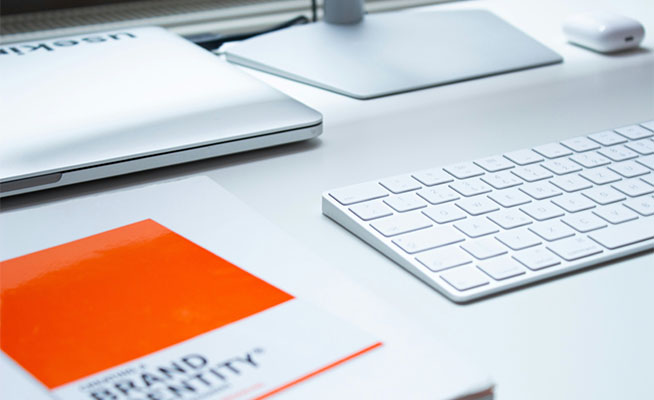 Table top with a Mac, and a brand identity book. 