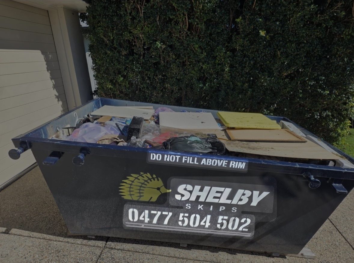 A Shelby Skips bin of household rubbish on a driveway in front of a garage