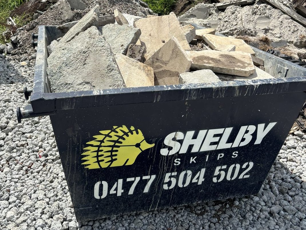 A Shelby Skips 2m bin of broken concrete slabs on gravel.