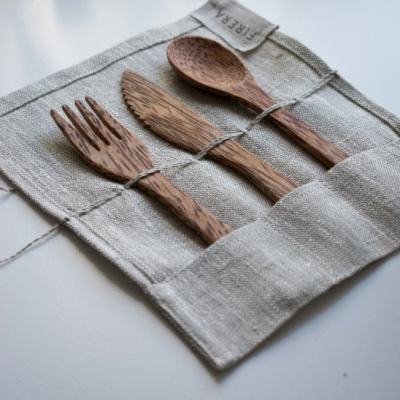 A wooden fork, knife and spoon tucked into the pockets of a rolled linen cutlery wrap tied with string.