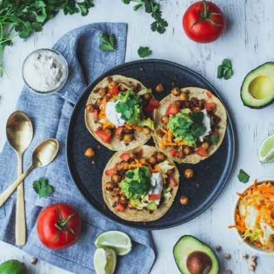 An overhead view of three chickpea tostadas topped with guacamole, tomato and coriander, with limes and avocado alongside.