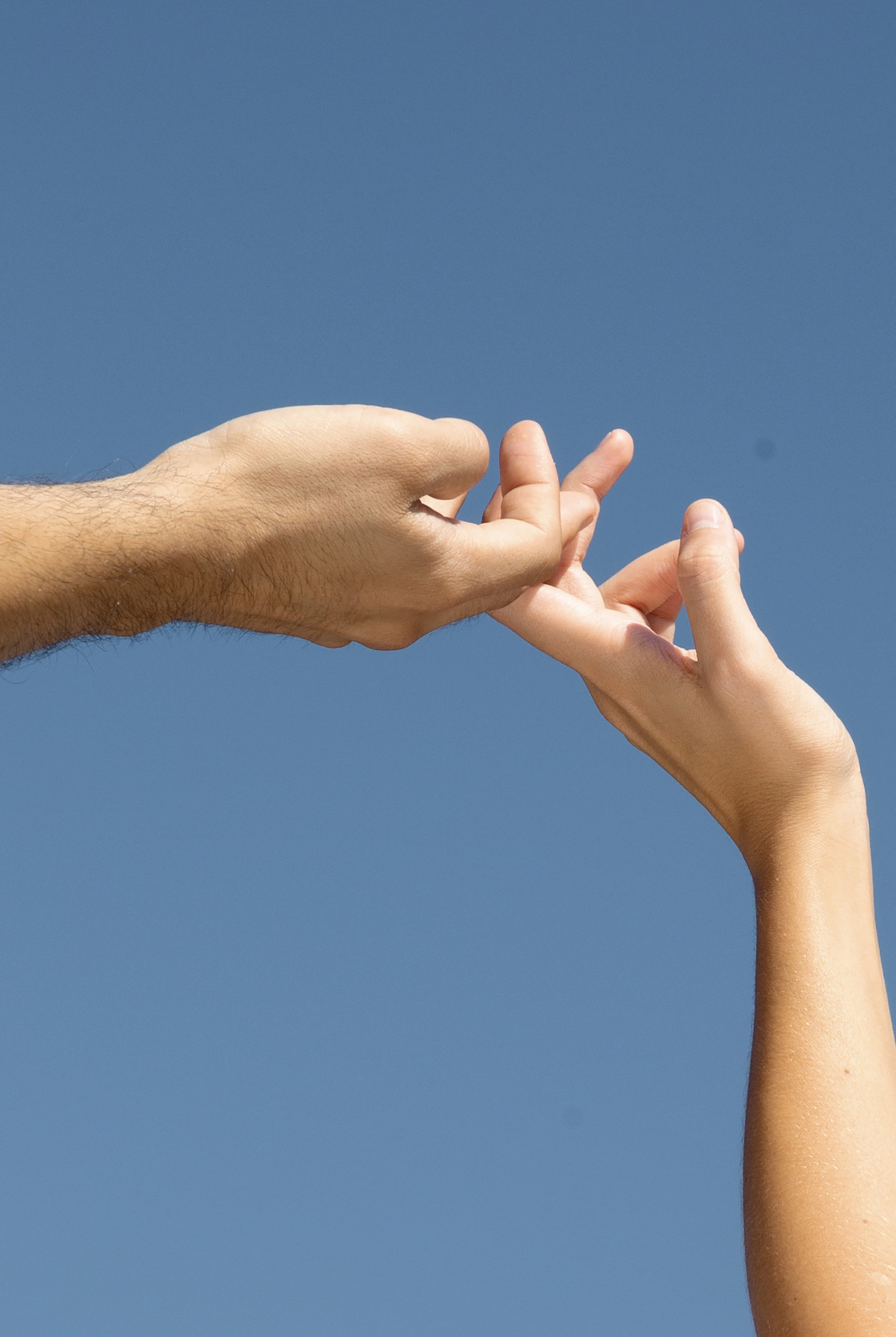 Couple's hands reaching together against a blue sky — intimacy and connection