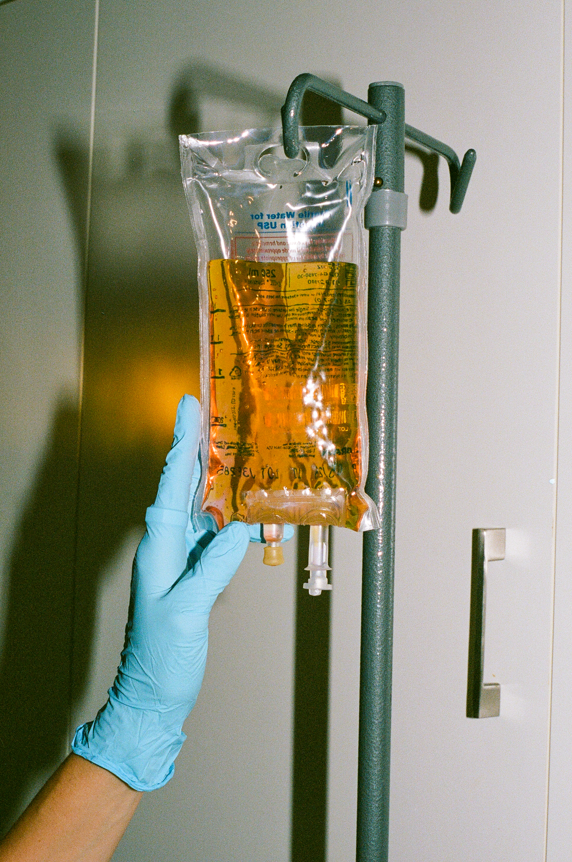Gloved clinical hand holding an amber IV bag on a stand — physician-supervised NAD+ therapy at Upper Room Clinic