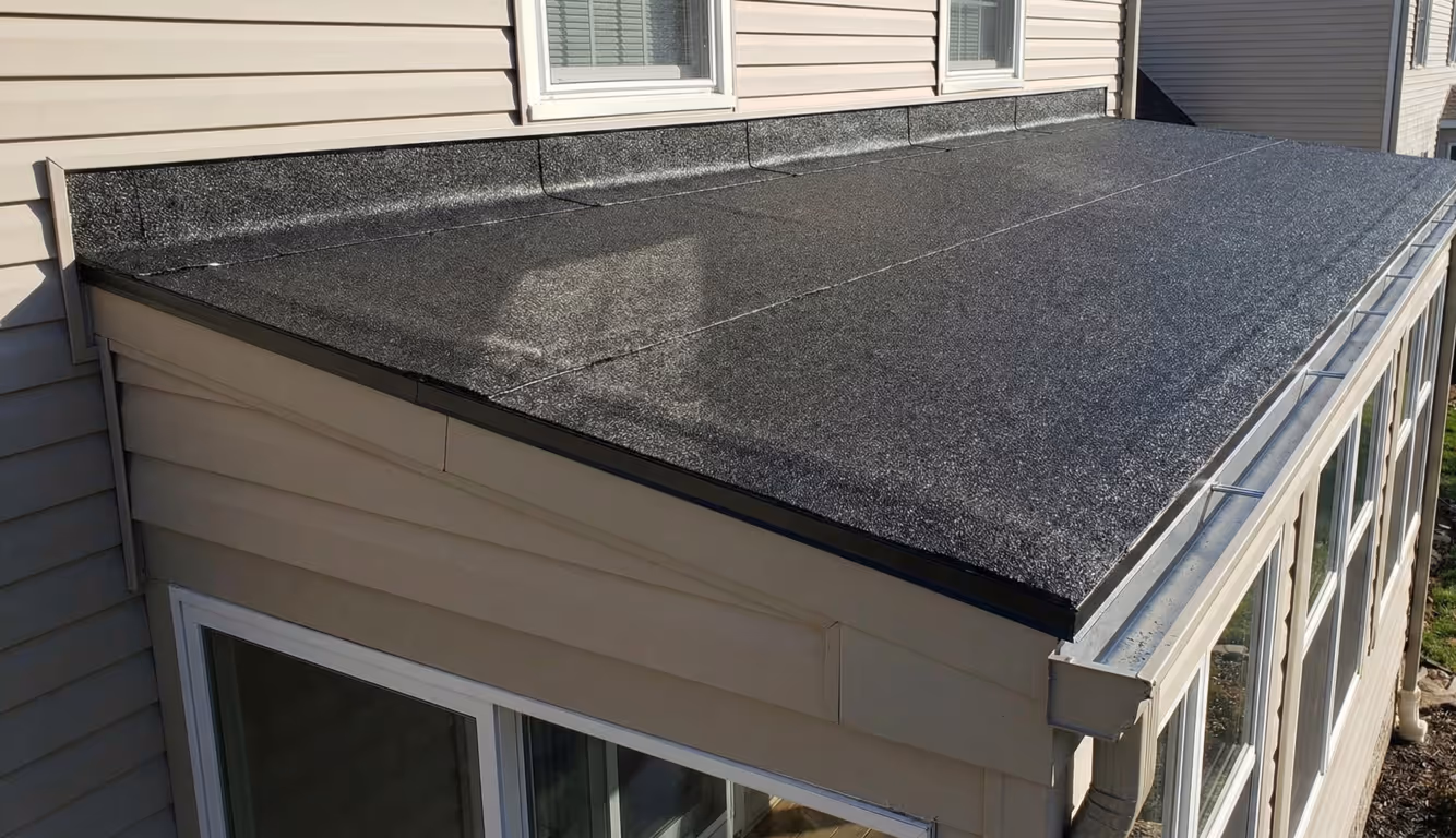 Flat black shingle roof on a beige house extension with white framed windows below.