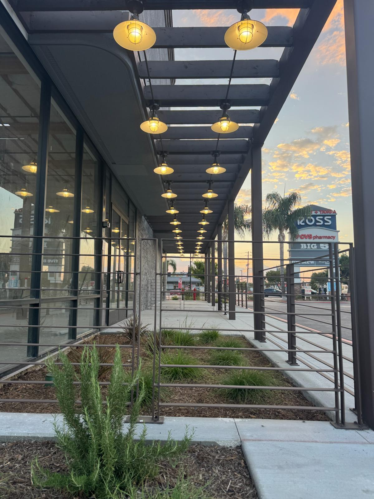 Commercial building renovation by Build Solutions in Los Angeles featuring outdoor trellis with modern lighting, landscaping, and new glass storefront.