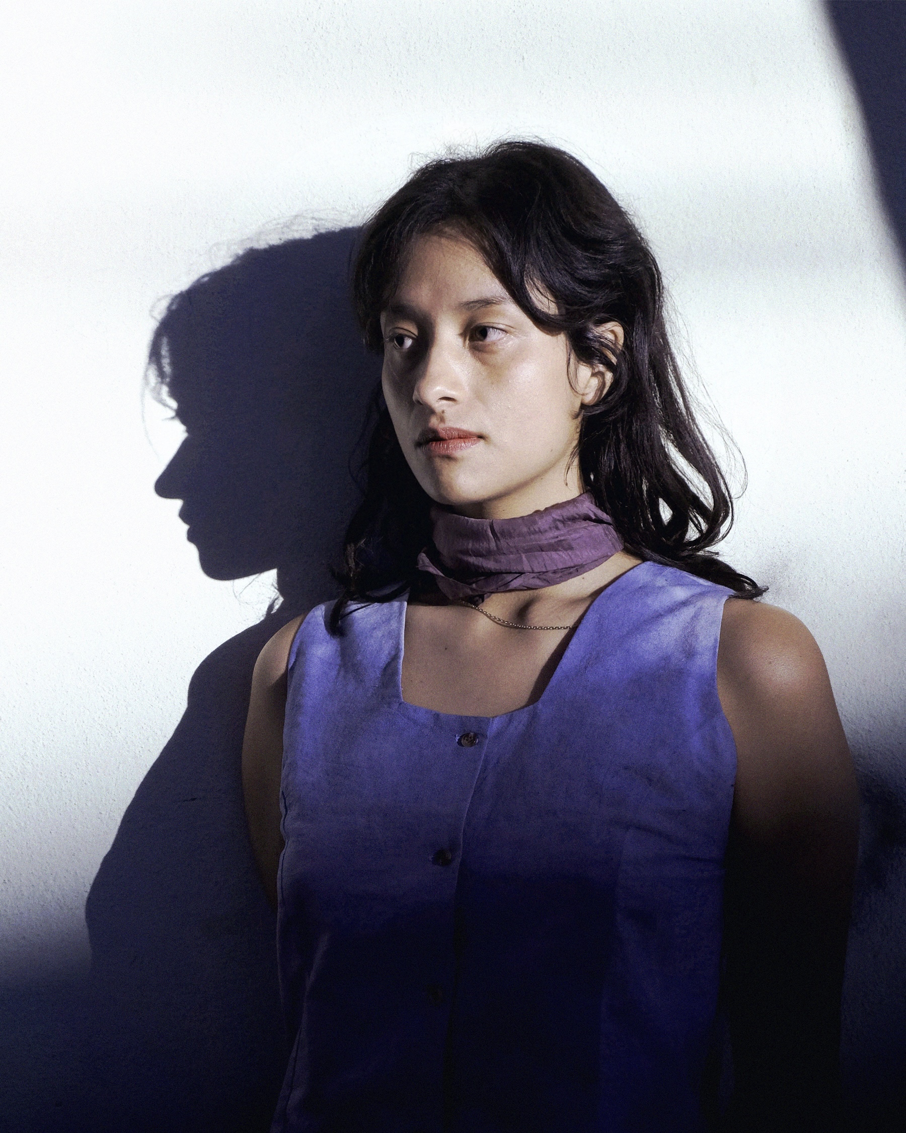 Vica Pacheco stands at centre slightly facing towards her right, under a bright spotlight that casts a shadow of her profile