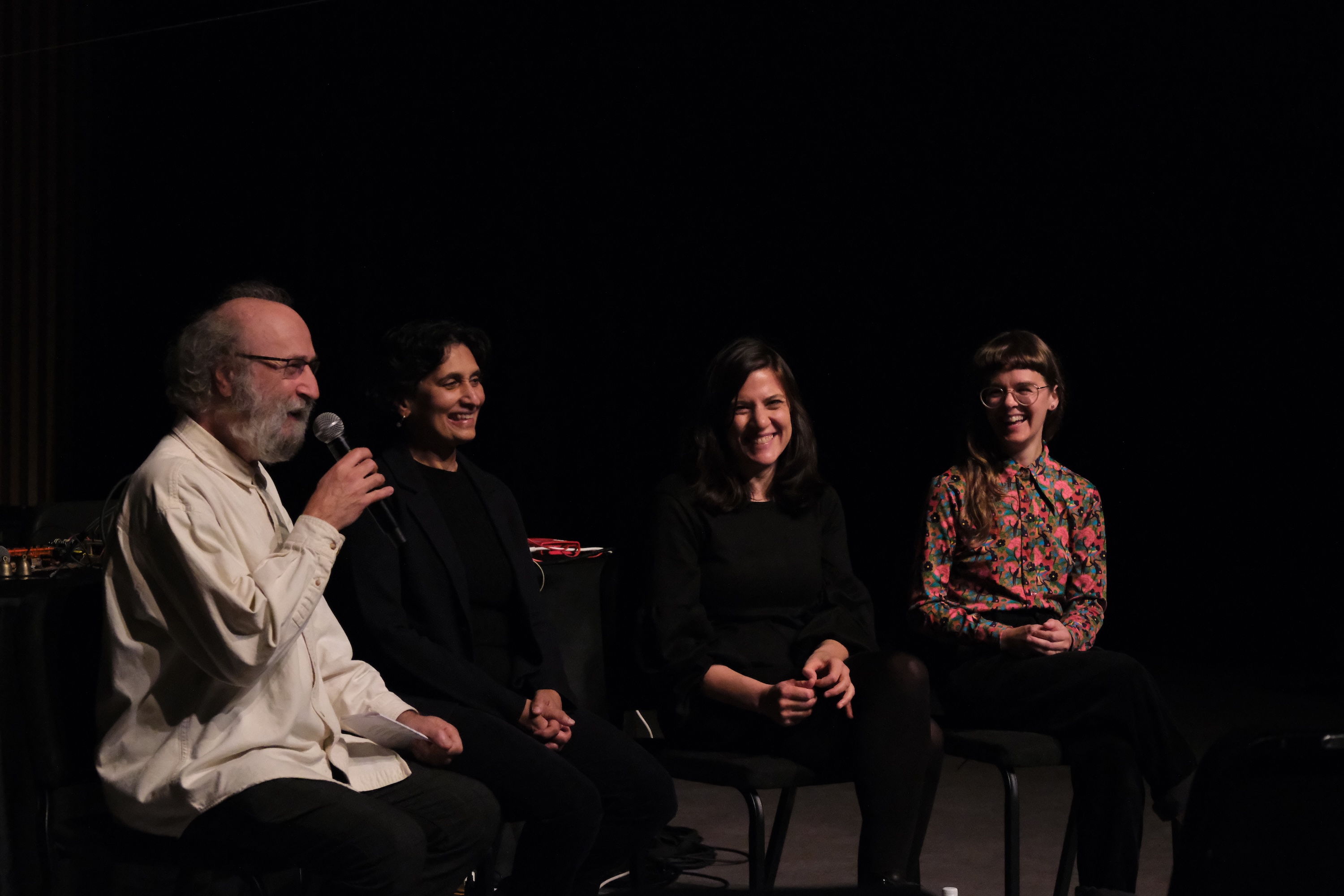 Émilie Payeur, Parmela Attariwala, Cecilia Lopez, and Giorgio Magnanensi sit on stage in chairs; Giorgio on the left speaks into a microphone while Émilie, Parmela, and Cecilia next to him smile and listen.