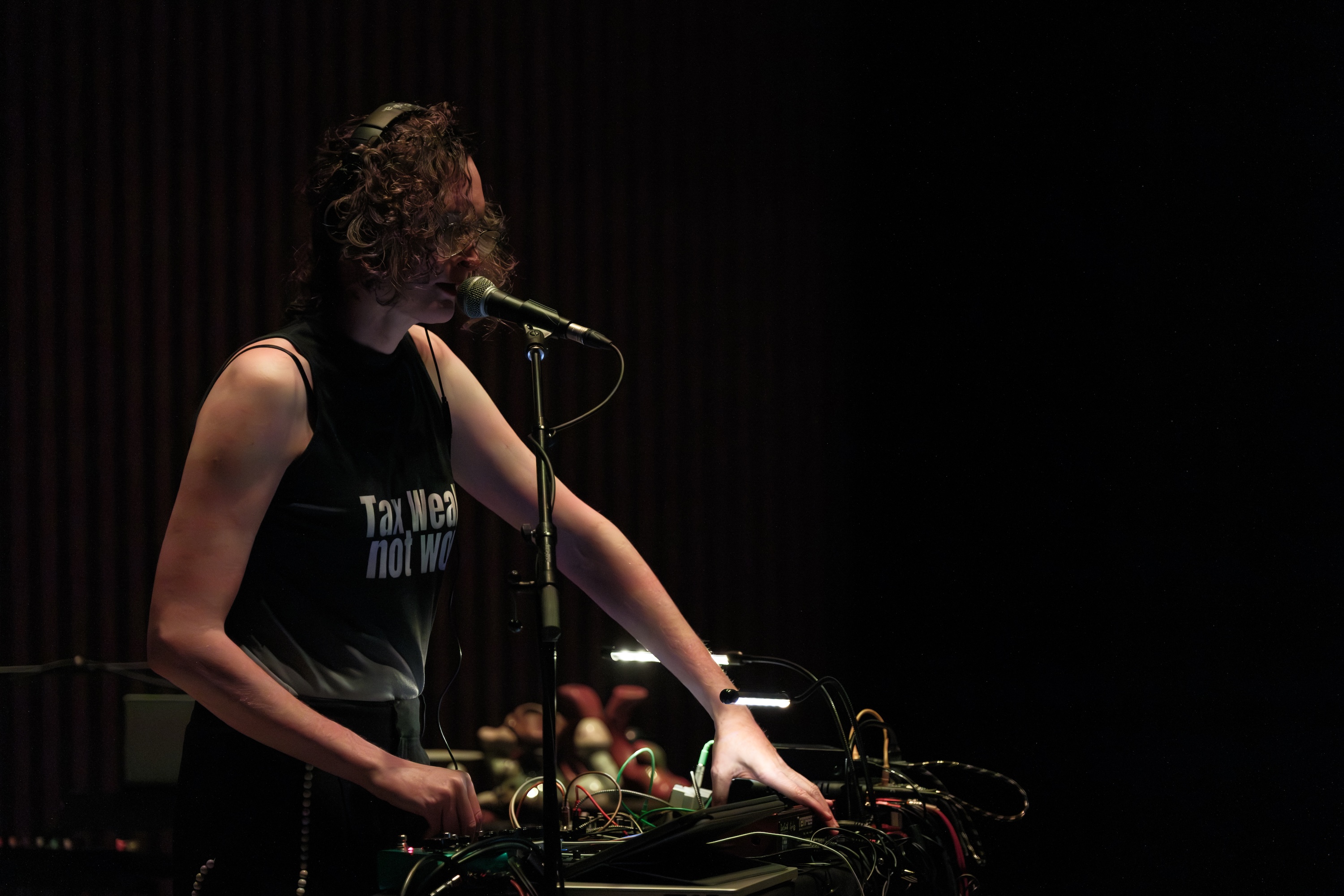 Brady Marks wearing headphones and a shirt stands at a microphone, adjusting audio equipment in a dimly lit setting.