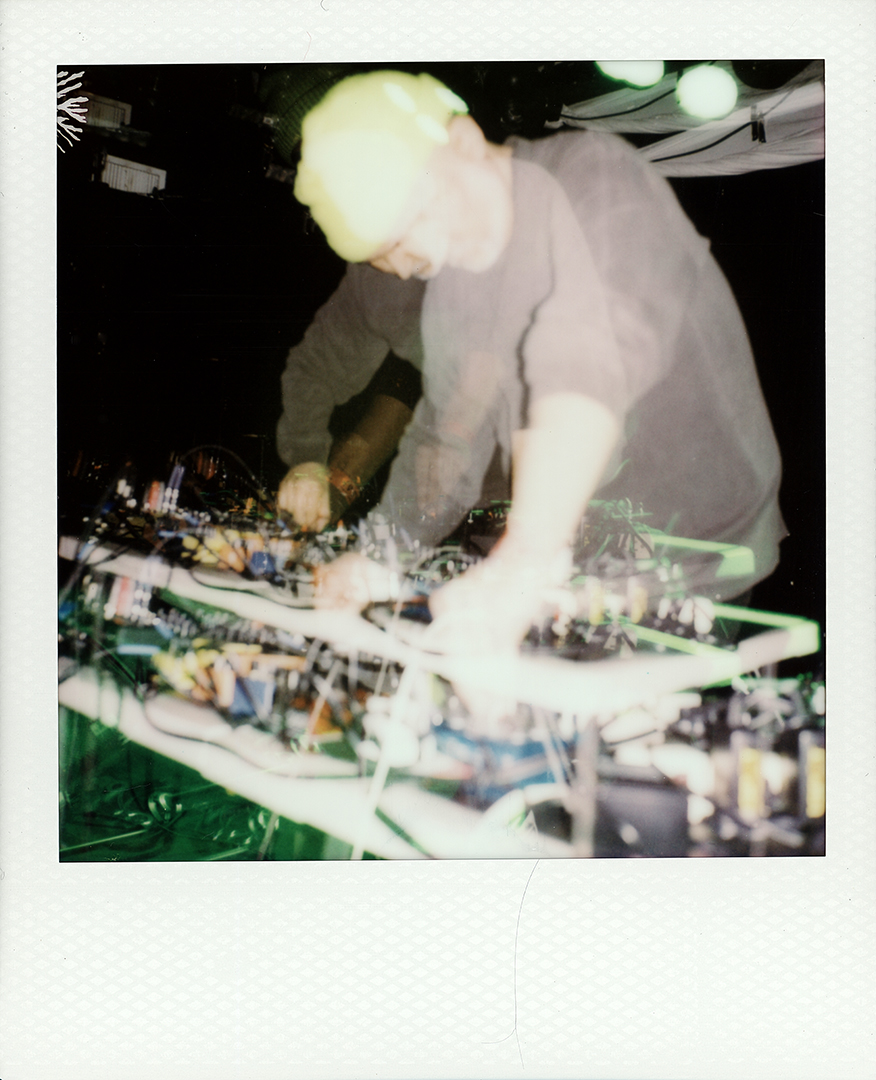 A multiple exposure photograph of Jarrett Martineau standing at a table full of pedals and patch cables.