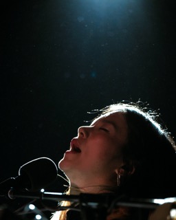 Charmaine Lee passionately performing under a spotlight, with eyes closed and face tilted upwards and dark background