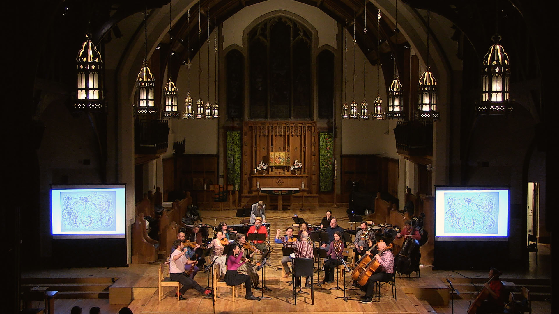 A group of musicians performs in a grand indoor space, with an altar in the background, large windows, and screens displaying visuals.