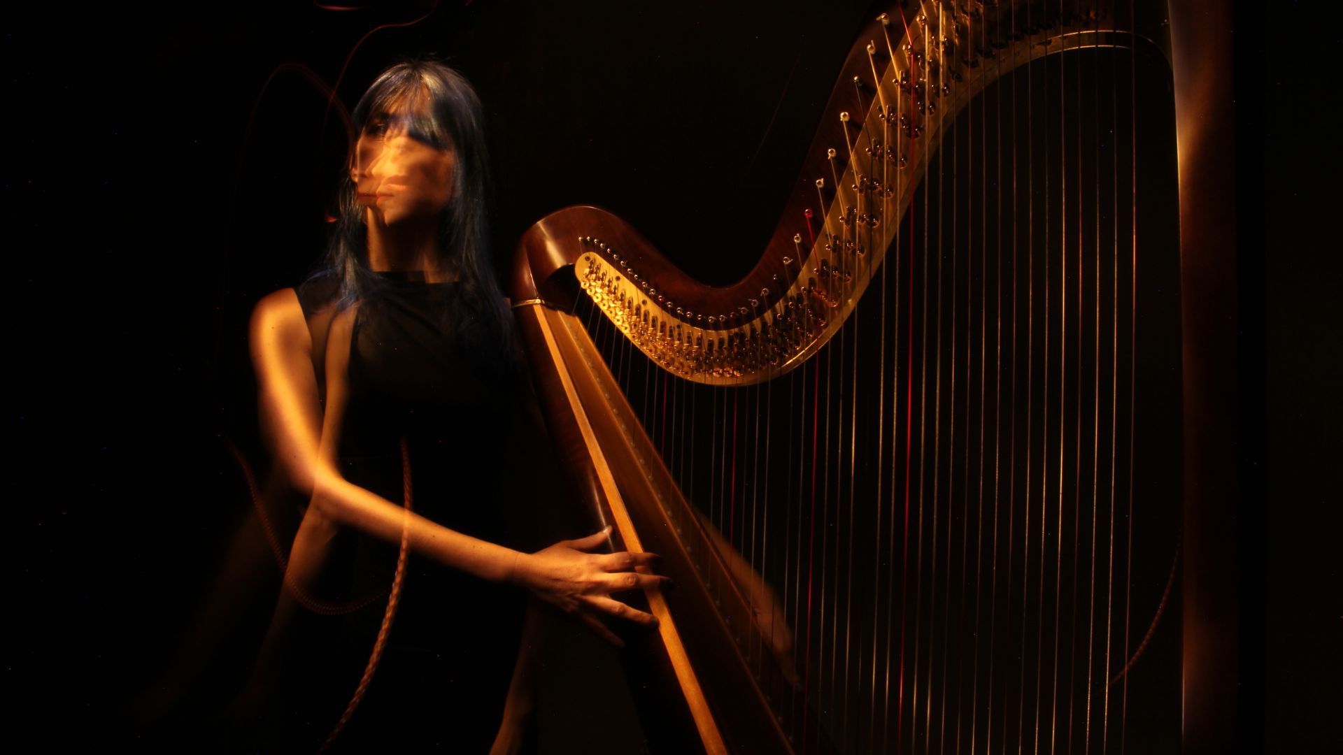 A person with bangs and long hair stands beside a harp in dim lighting, with motion blur effect on their face and arm, creating a dynamic and artistic scene.