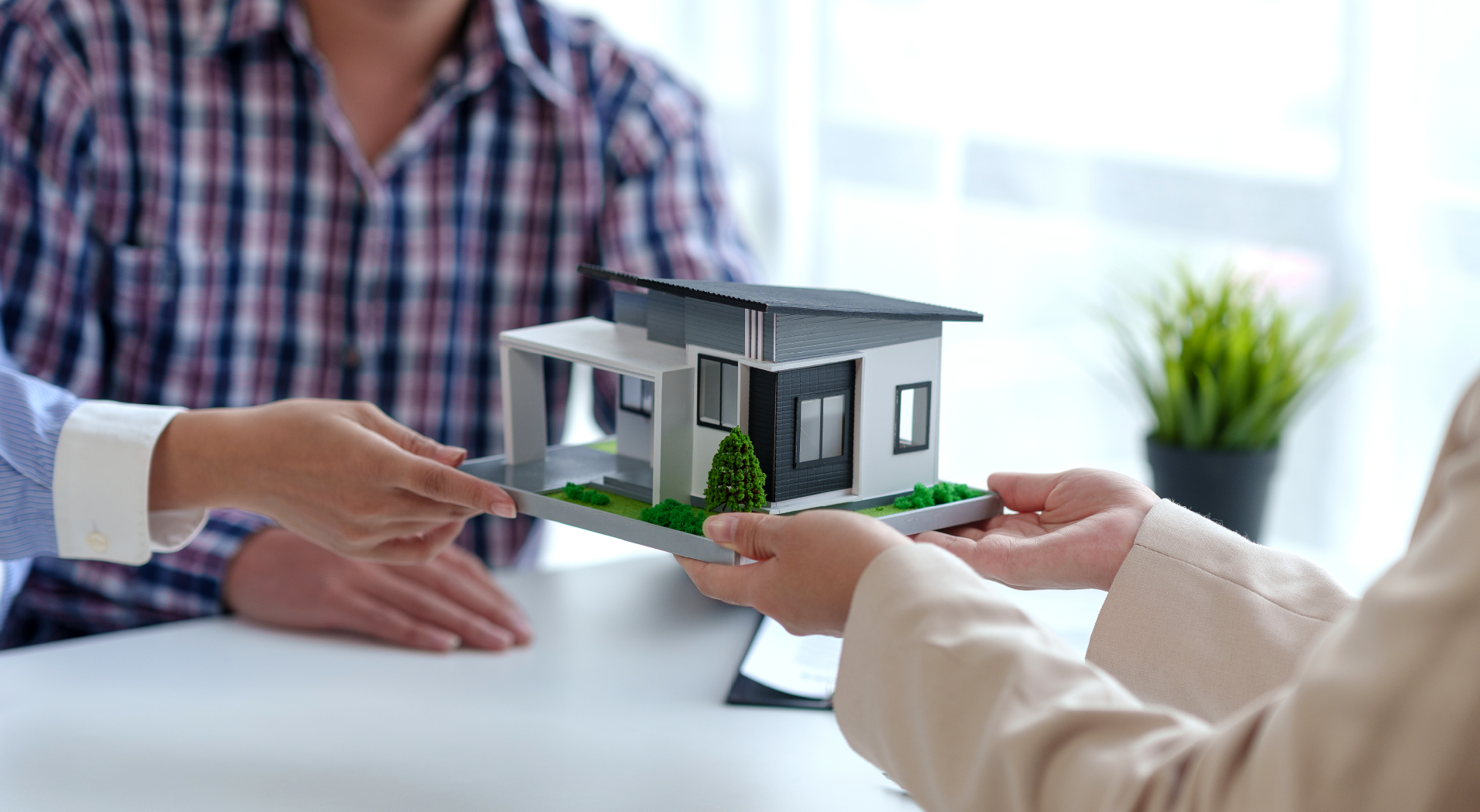 Two people exchanging a detailed model of a modern house at a table.