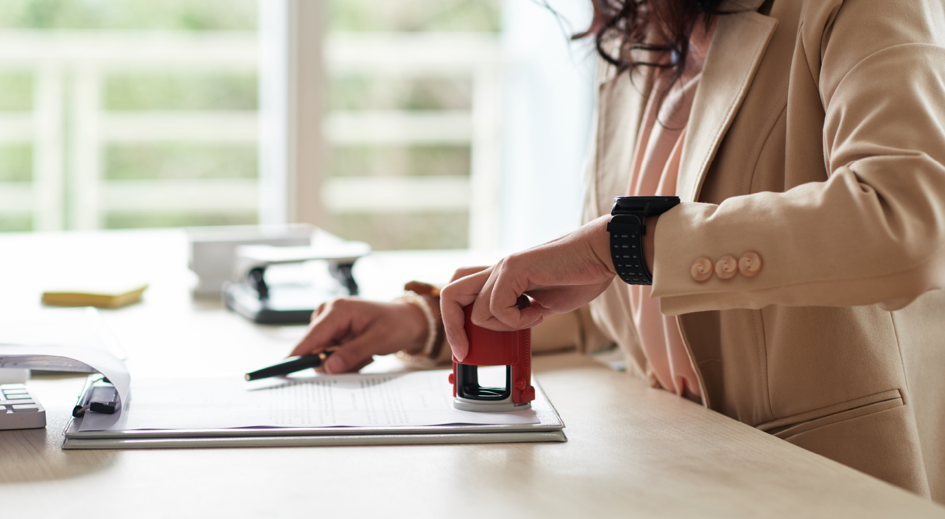 Person stamping a document on a desk with natural light in the background.