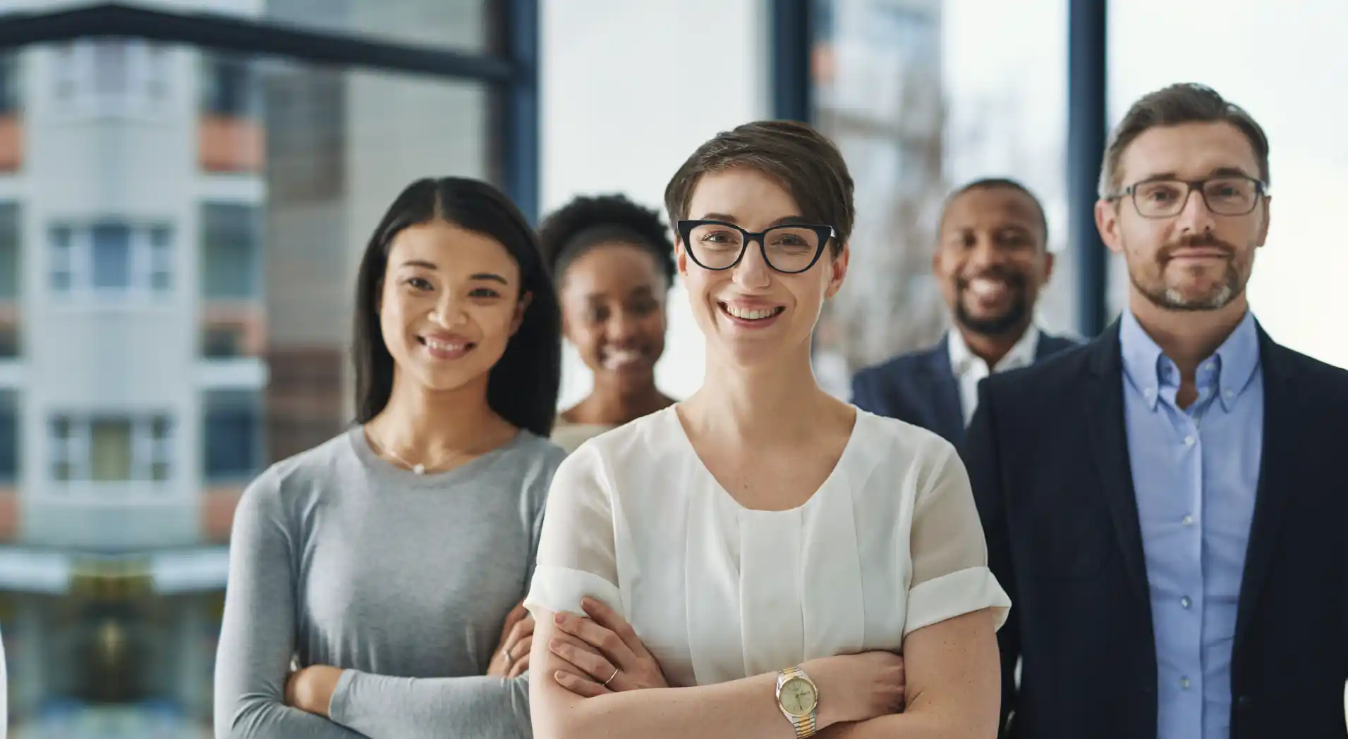 Diverse group of five smiling professionals standing indoors with arms crossed.