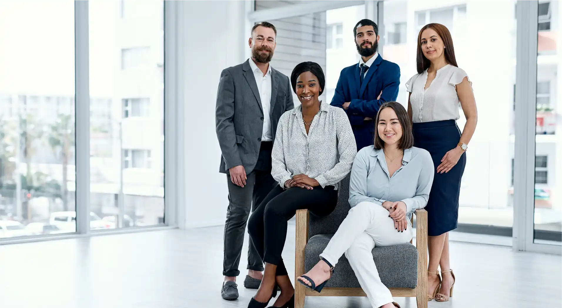 Diverse group of five business professionals posing confidently in a bright modern office.