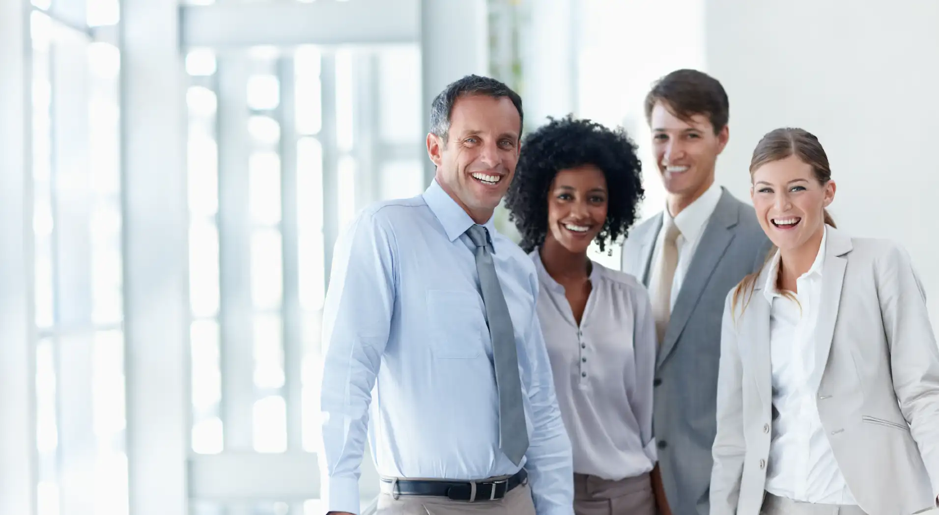 Four diverse business professionals smiling and standing together in a bright modern office.