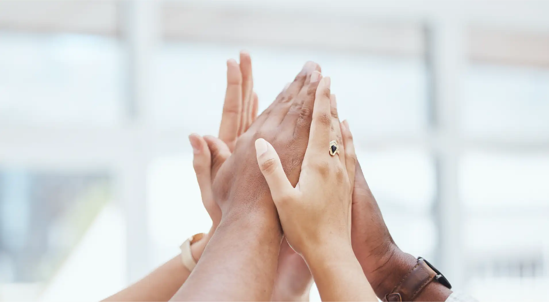 Multiple hands of diverse individuals stacked together in a group high-five gesture.