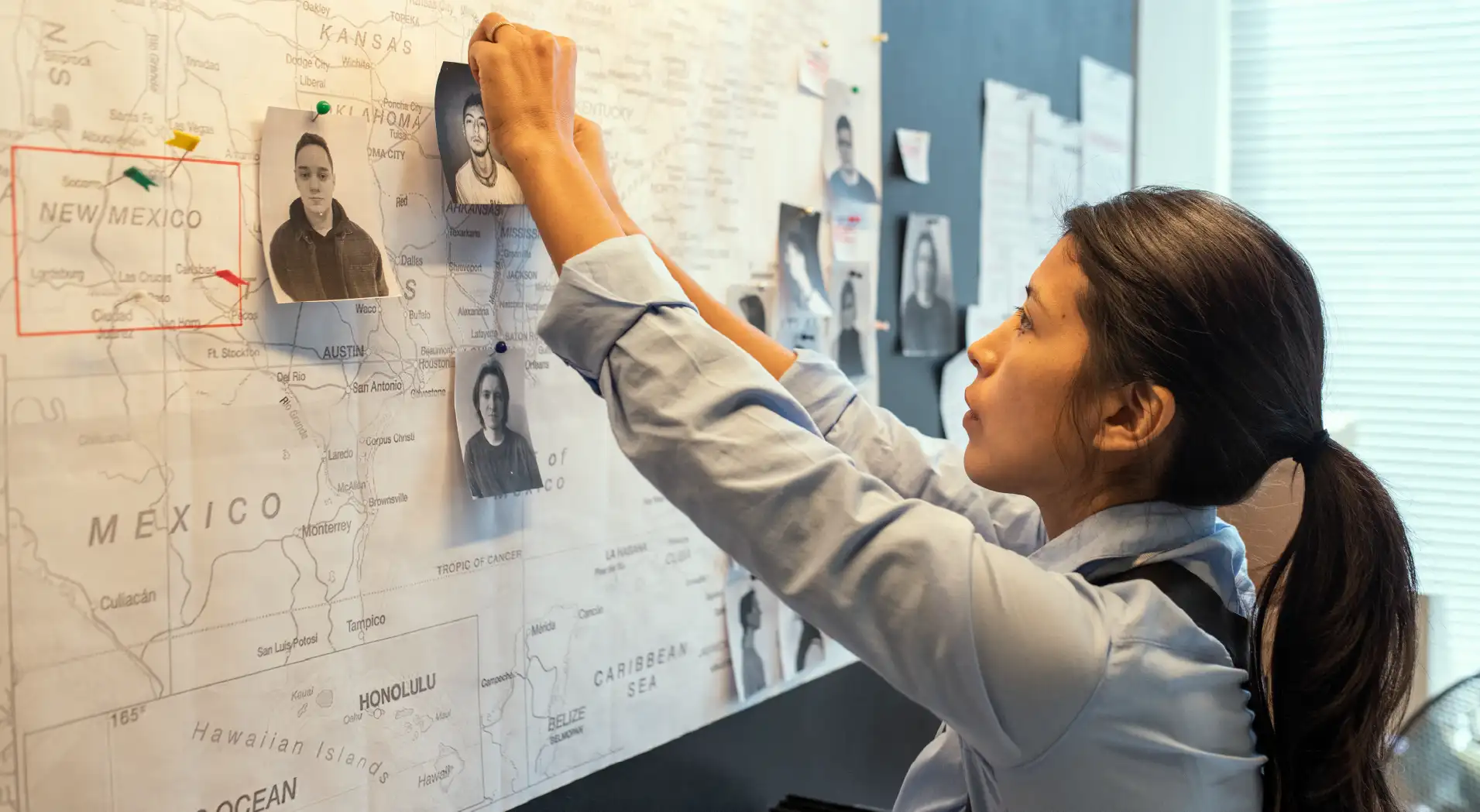 Woman pinning black-and-white photos of people on a large map showing the southern United States and Mexico.