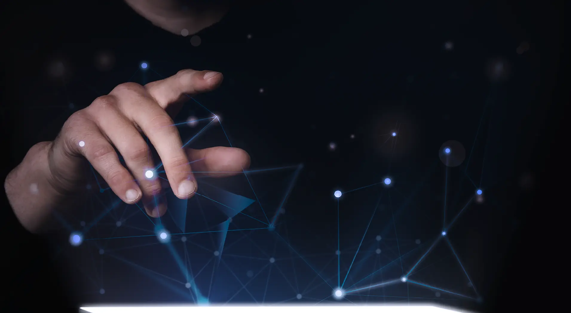 Hand interacting with glowing connected blue dots and lines above a bright surface against a dark background.