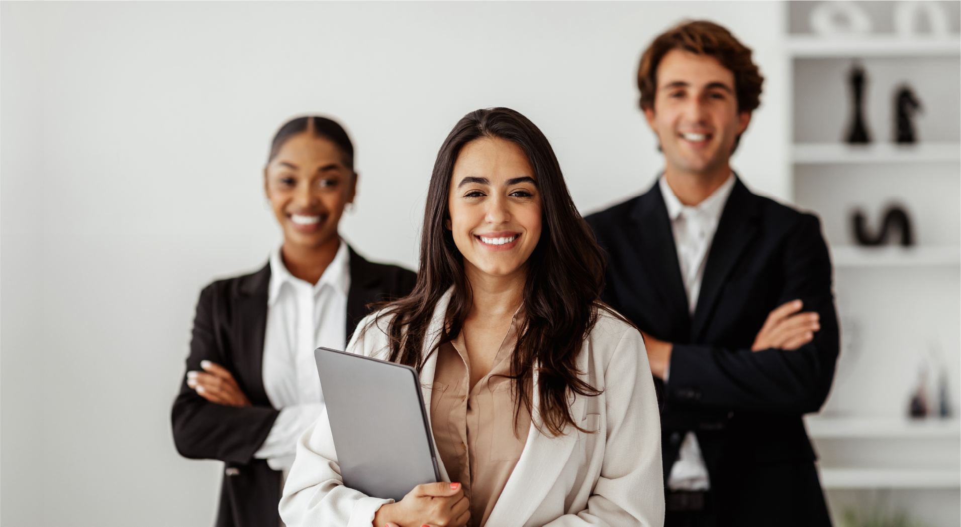 Smiling professional woman holding a tablet with two colleagues standing confidently behind her in an office.