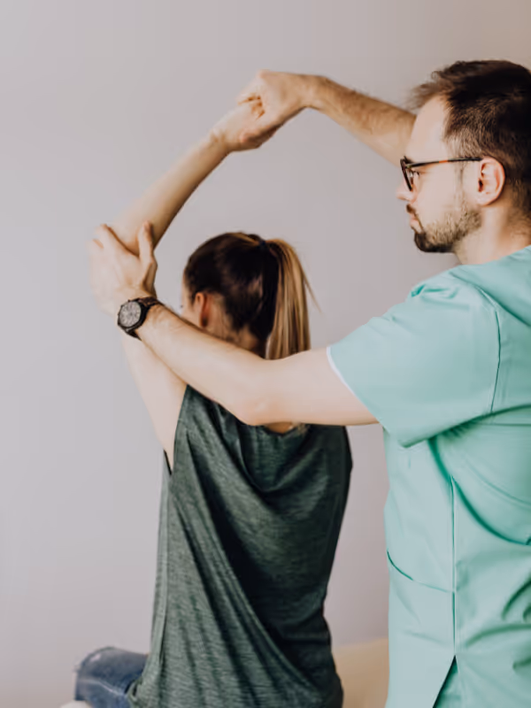Physical therapist assisting woman with arm stretching exercise.
