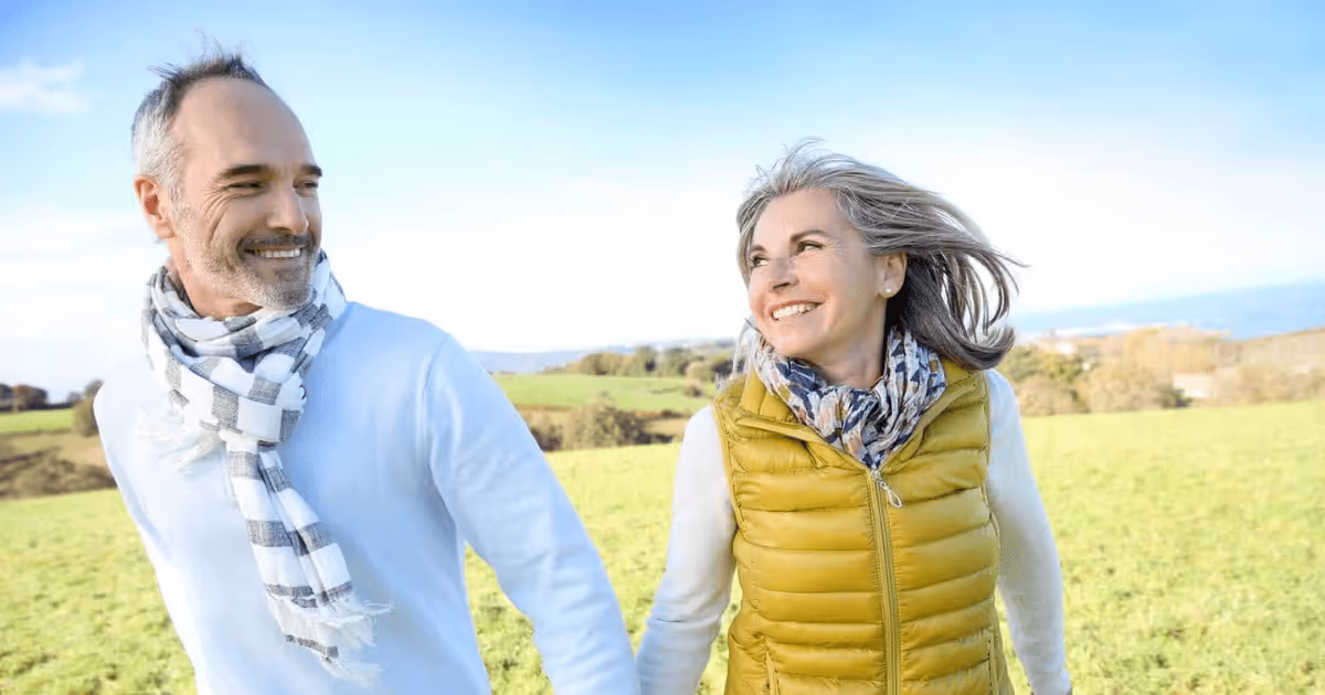 Smiling older couple holding hands and walking outdoors in a green field on a sunny day.