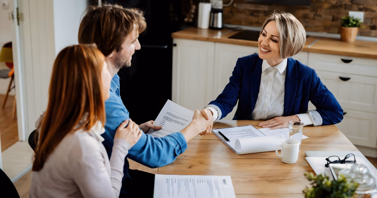 Happy agent shaking hands with young couple after successful meeting