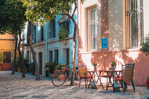 Colorful cobblestone street with pastel buildings, red bicycle, outdoor café table, and potted plants.