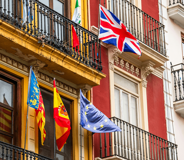 Colorful building with balconies displaying flags of UK, EU, Spain, and Valencian Community