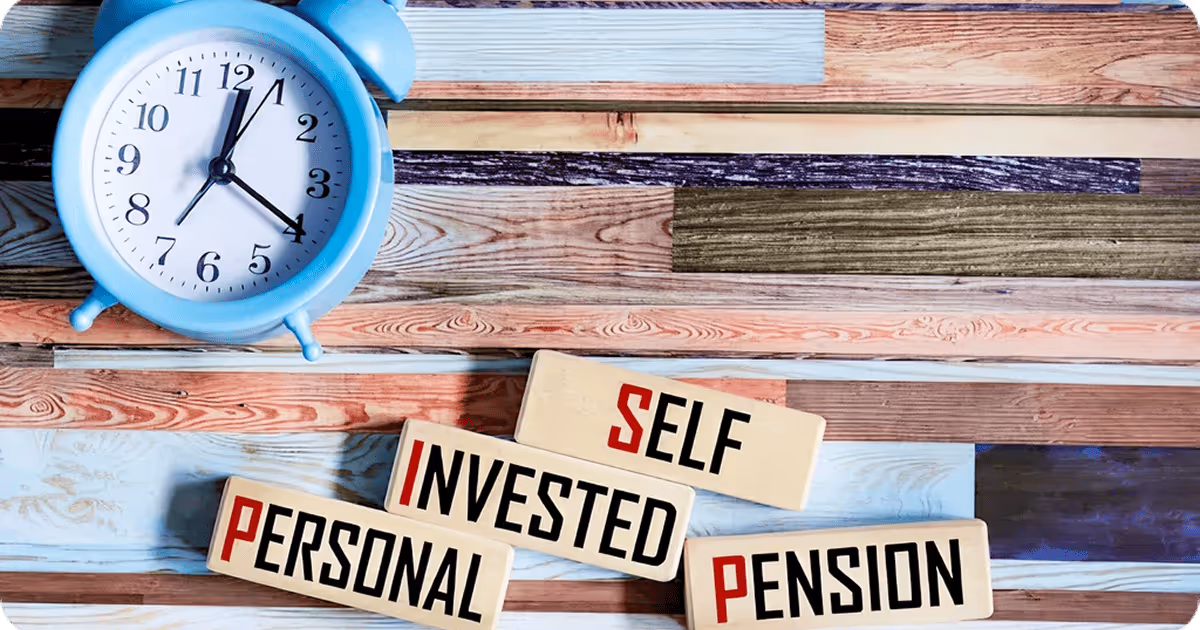 Blue alarm clock beside wooden blocks with the words " Self Invested Personal Pension.”