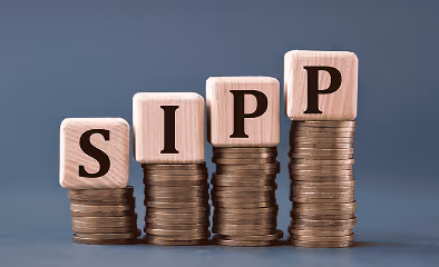 SIPP (Self Invested Personal Pension) - acronym on wooden cubes on coins on a gray background. Business concept