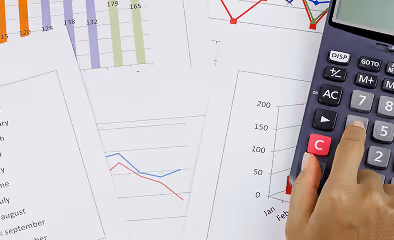 Hand using a calculator on top of financial charts and graphs, representing investment analysis and financial data review.