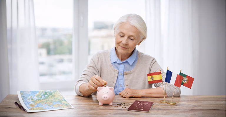 Senior woman saving coins in piggy bank with passport, world map, and Spain, France, Portugal flags on the table