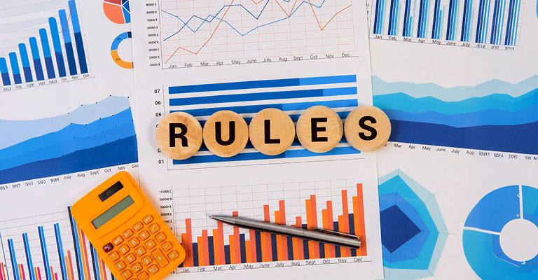 Wooden discs spelling 'RULES' placed on financial reports with charts, graphs, calculator, and business analytics documents representing non-residence rules and financial planning.
