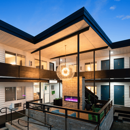 Patio de un motel moderno de estilo de mediados de siglo al atardecer, en el que se ven habitaciones iluminadas, pasillos exteriores a oscuras y una lámpara decorativa con forma de estrella.