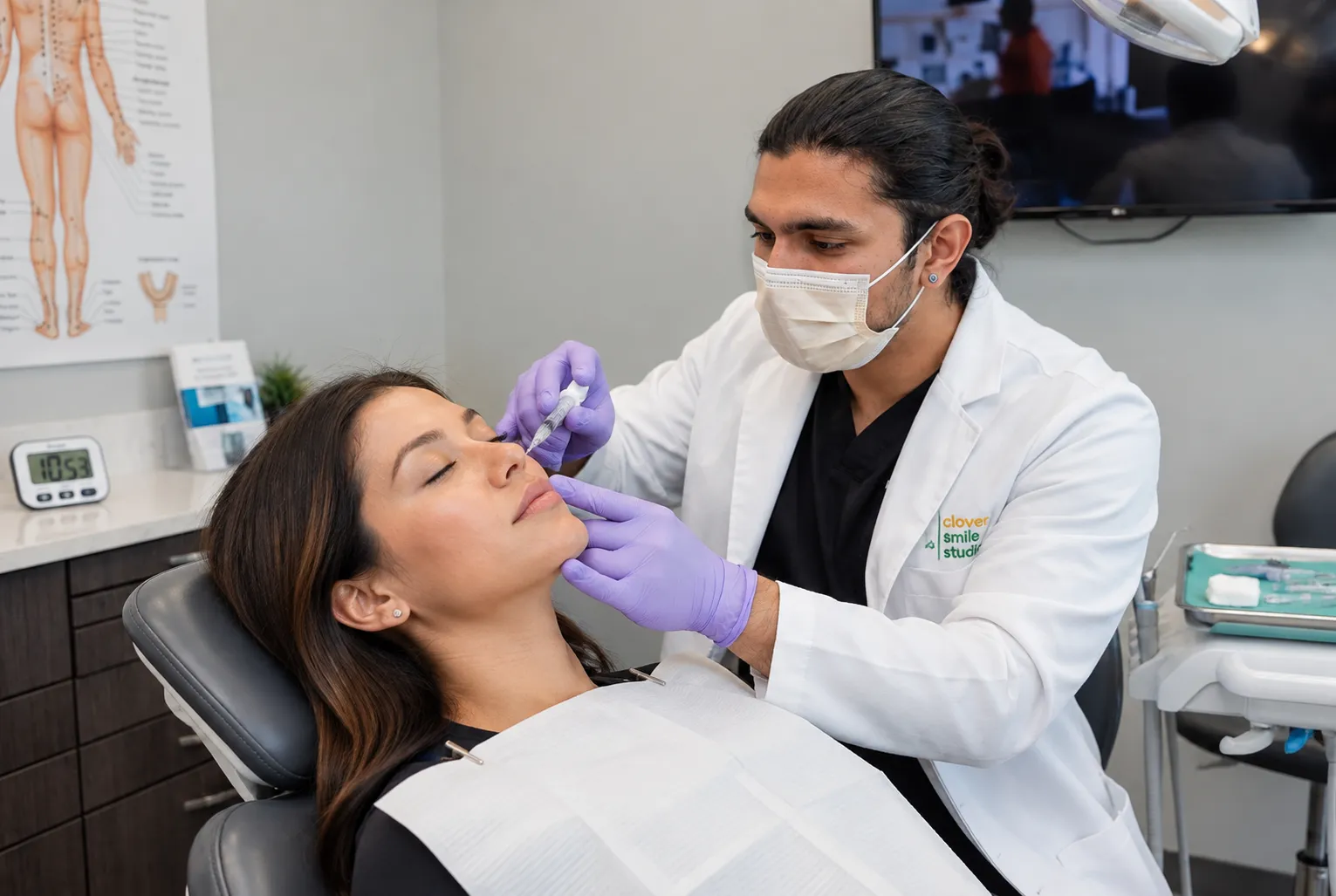 Dentist wearing a face mask and purple gloves performing a facial esthetic treatment on a male patient at Clover Smile Studio.