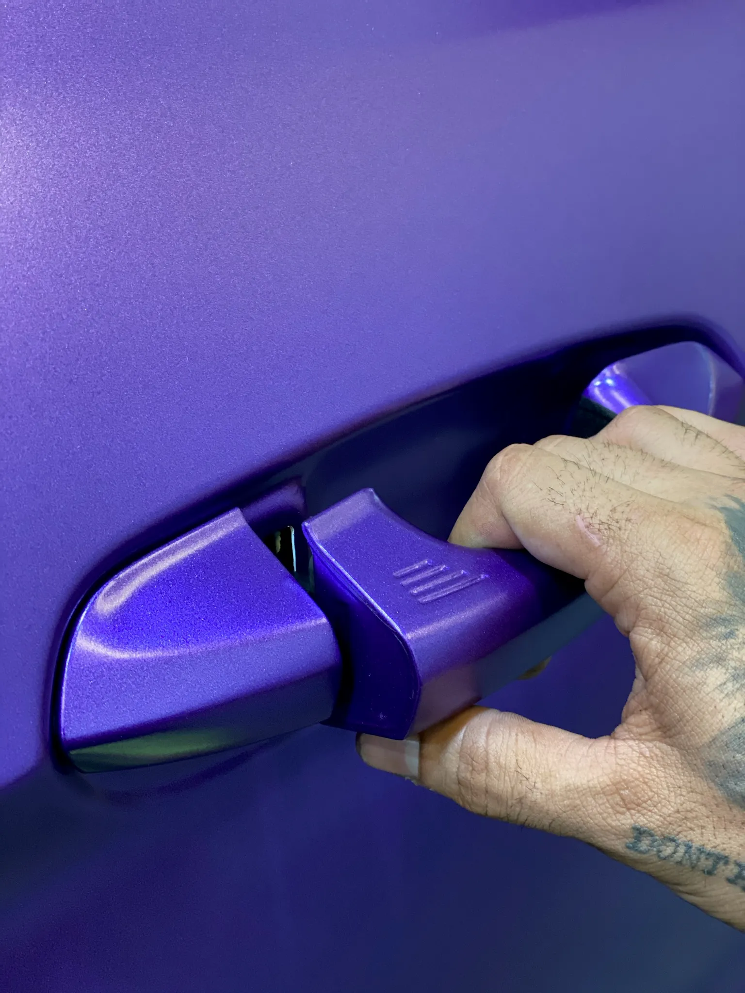 Hand opening a purple car door handle at Allure Auto Spa.