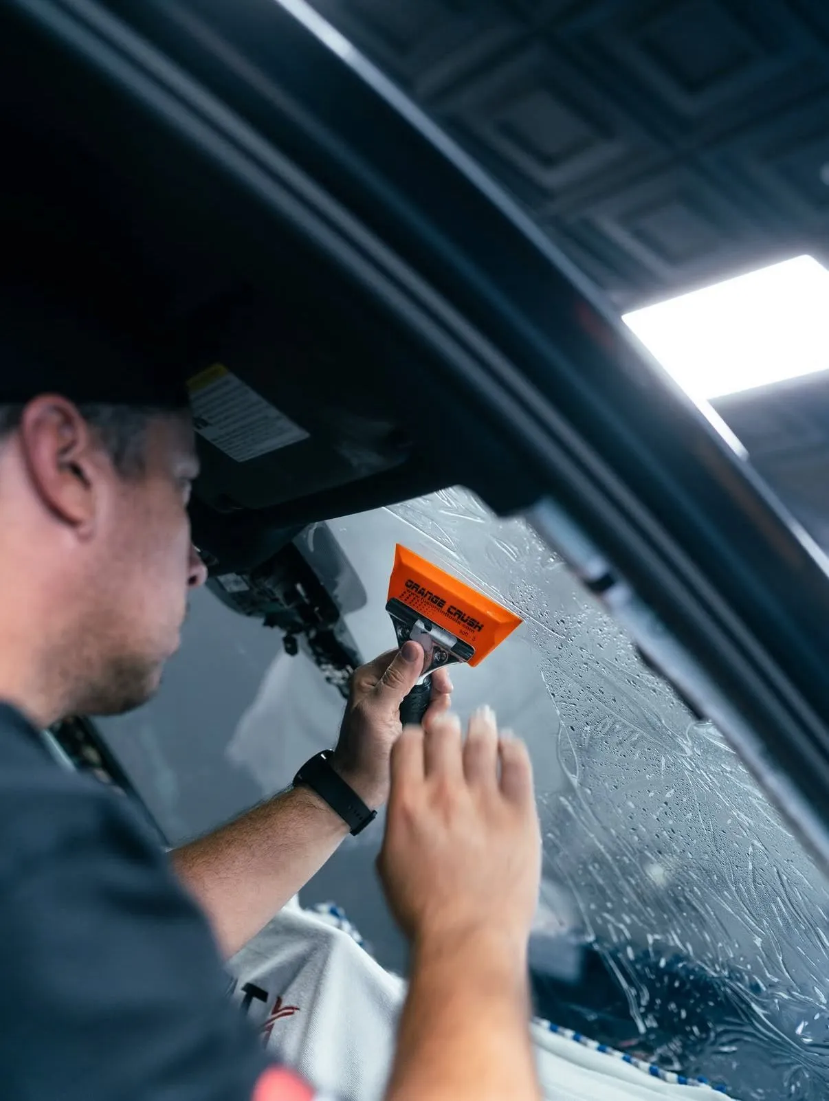Installer squeegeeing window tint film onto a car door glass at Allure Auto Spa, Fern Park FL