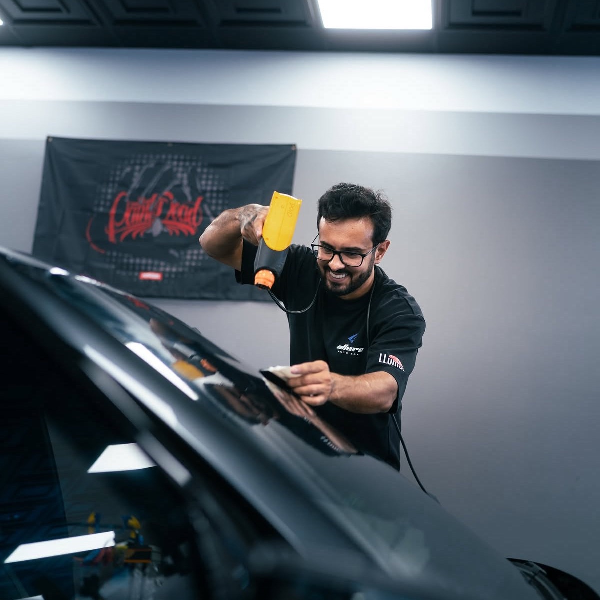Allure Auto Spa installer applying ceramic window tint film to a car windshield