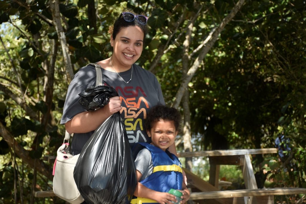 Smiling woman holding a full trash bag next to a young boy in a life jacket