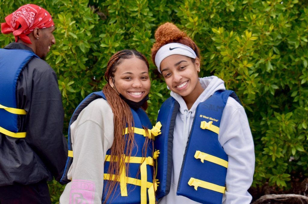 Two smiling young women in life jackets in front of mangroves
