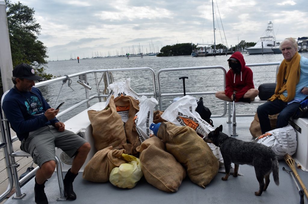 Volunteers and a dog aboard a boat with burlap sacks and bags full of collected litter