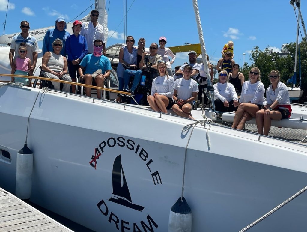 Group of crew and guests, including wheelchair users, aboard the Impossible Dream catamaran at the dock