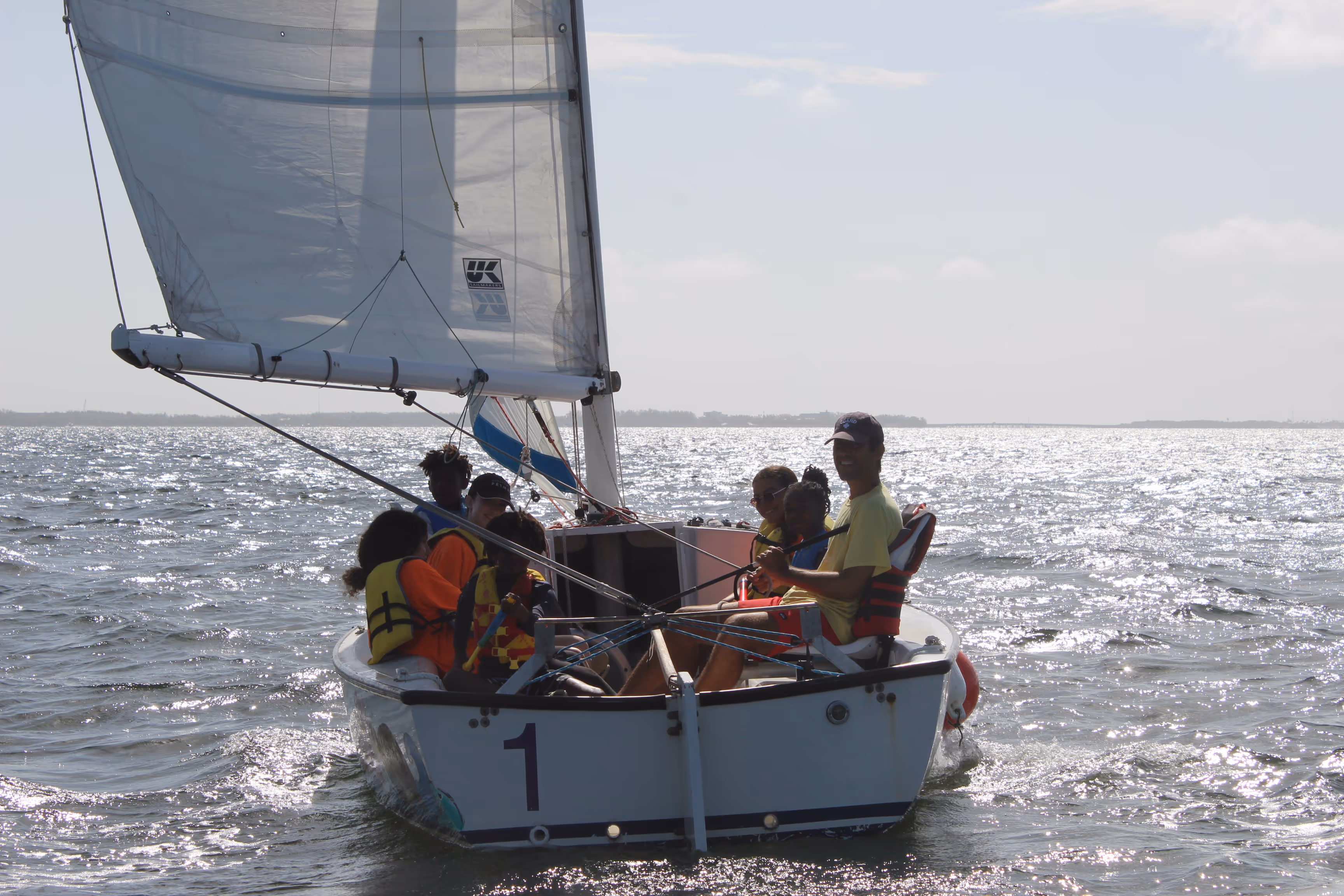Five people sailing a keelboat under full sail on a bright day